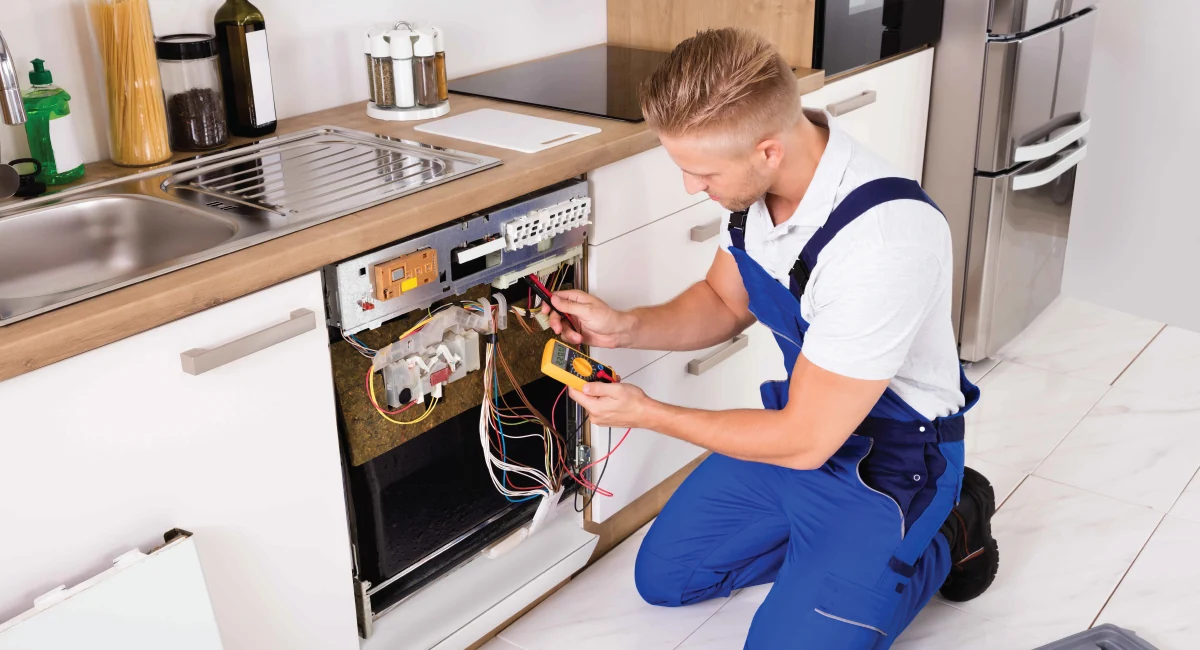 Appliance technician testing exposed dishwasher wiring with a multimeter