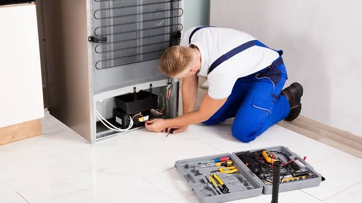 Technician repairing the rear compressor of a refrigerator with tools nearby