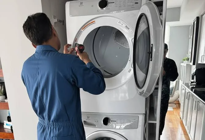 Technician repairing the upper dryer in a stacked laundry appliance pair