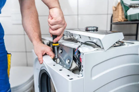 Close-up of a screwdriver being used on an open washing machine top panel