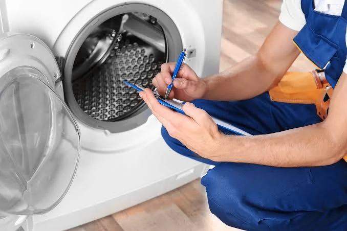 Technician recording notes beside an open front-loading washing machine